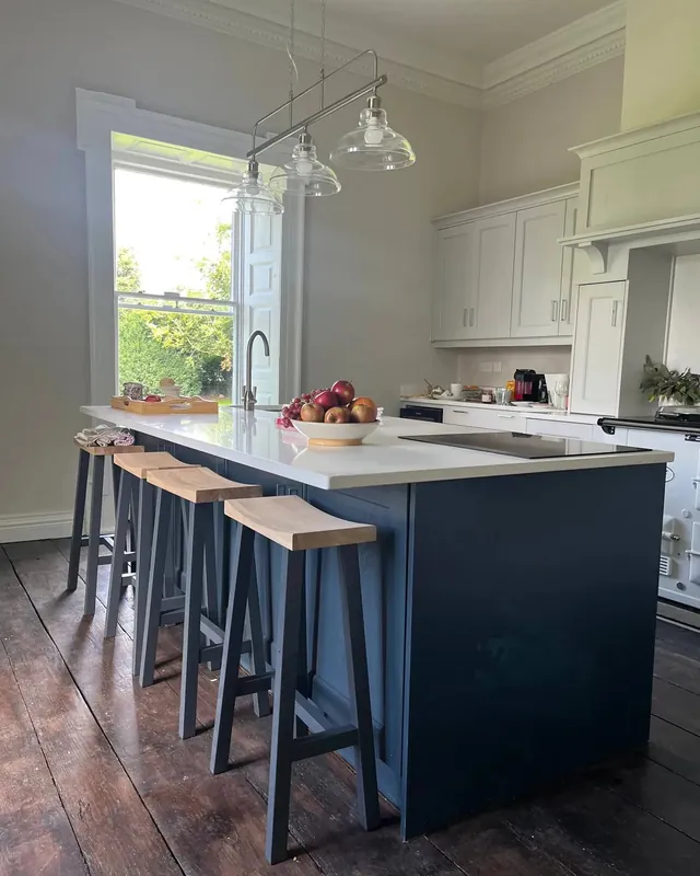 The kitchen at Mountrothe House: a navy island with stools under glass pendant lights